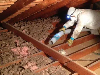 Technician removing damaged attic insulation with a vacuum hose